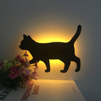 OptiLair cat-shaped acrylic night light with warm yellow sound-sensor glow on a bedroom wall