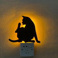 OptiLair cat-shaped acrylic night light with warm yellow glow and sound-sensor activation on a wall outlet.