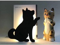 OptiLair black dog silhouette night light with sound sensor, casting a warm glow behind a decorative cat figurine.