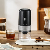 OptiLair portable electric coffee grinder in black with a clear powder silo and textured silver grip on a wooden table
