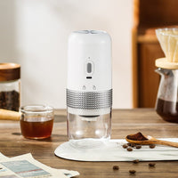OptiLair portable electric coffee grinder in white with a clear powder silo and textured silver grip on a table.