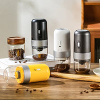 OptiLair portable electric coffee grinders in black, white, grey, and yellow with clear powder silos on a wooden table